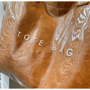 Detail of glossy brown tote bag featuring wrinkled texture and white TOTE BAG printing