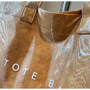 Detail of glossy brown PVC tote bag with wood grain texture and printed TOTE BAG text