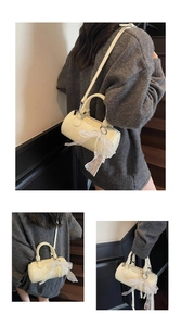 Detail view of cream cylinder bag with white lace bow, pearls, and fashion branding