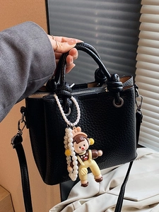 Litchi texture black bucket bag with a pearl doll charm shown in a handheld view