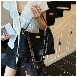 Detail of black quilted leather bucket bag with gold chain handles and metal twist lock