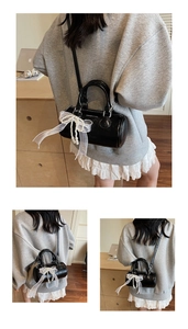 Detail of black cylinder bag with white lace bow and pearl charm in home setting