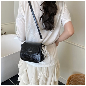 Detail of black leather crossbody bag featuring lace bow and pearl charm accessory