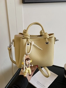 Yellow pebbled leather bucket bag with pearl chain and cartoon pendant in 45-degree view
