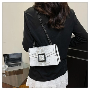 Détail du petit sac blanc à motif serpent avec bandoulière chaîne sur un bureau moderne