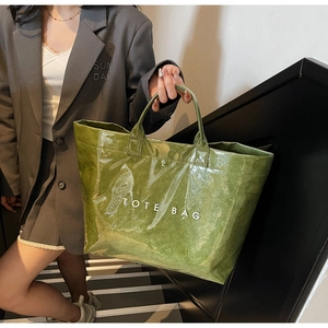 Detailed view of large green tote bag with glossy crinkled texture and white logo print
