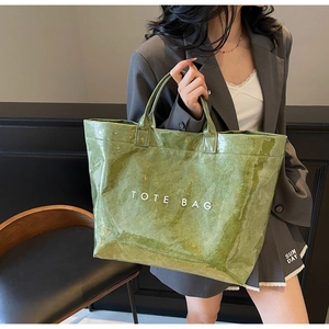 Detail of green tote bag with crinkle texture and white lettering held by model