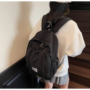 Detail of minimalist black nylon backpack featuring drawstring front pocket and logo label