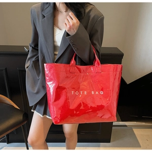 Detail view of glossy red PVC tote bag with white TOTE BAG lettering and sturdy handles