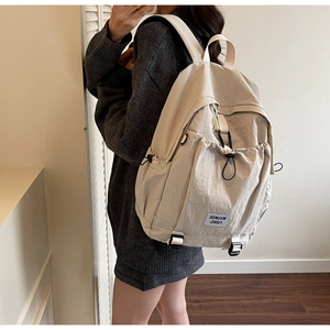 Close-up of minimalist beige nylon backpack with drawstring pockets and buckle detail