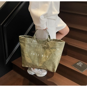 Detail of dark green tote bag with crinkle texture and white printed text on stairs