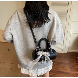Detail of black cylindrical bag featuring white lace bow and elegant pearl charm