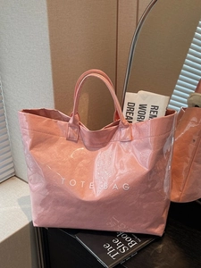 Pink glossy tote bag with crinkle texture and white TOTE BAG text in minimalist room