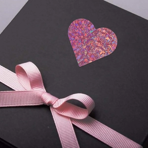 Dettaglio macro di adesivo olografico a cuore su scatola regalo nera con nastro rosa