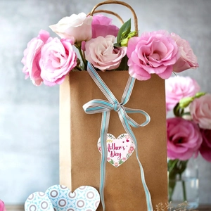 Close-up of Happy Mother's Day gift bag with fresh pink flowers and striped ribbon