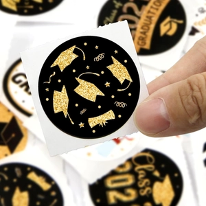 Roll of 500 graduation stickers with gold glitter mortarboard design on black background