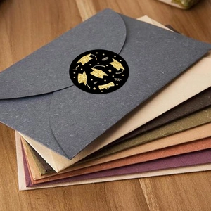 Close-up of black and gold graduation cap seal sticker on a grey envelope mailing