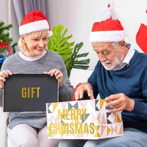 Elderly couple opening a festive Christmas gift box with gold Merry Christmas lettering