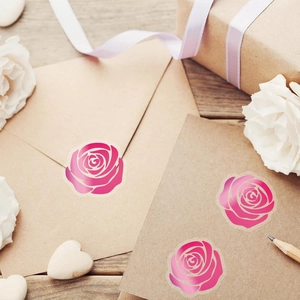 Adesivi con rose rosa che decorano una busta in carta kraft su un tavolo in legno