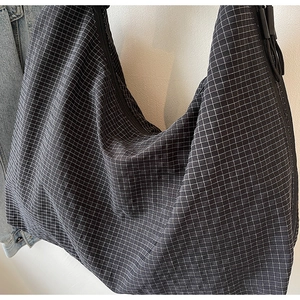 Détail d'un sac cabas noir à carreaux avec bandoulière réglable et fermeture éclair