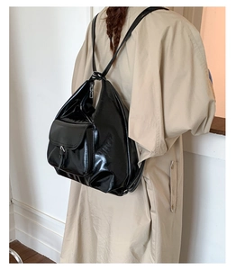 Detail of glossy black backpack with folding structure and metal buckle on trench coat
