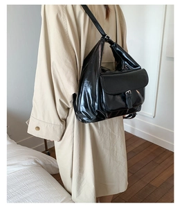 Detail view of black patent leather tote bag with silver buckle and glossy finish