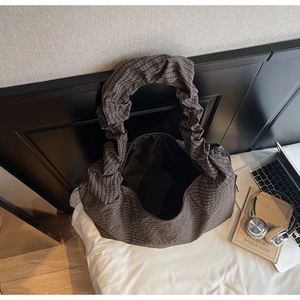 Vue de dessus d'un cabas à carreaux marron avec poignées plissées sur un lit blanc