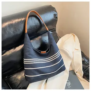 Detail of the navy canvas tote bag with white stripes and brown leather straps on a sofa