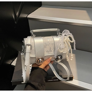 Détail du sac argenté pailleté avec chaîne de perles et nœud décoratif en dentelle