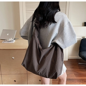 Side view of large brown checkered hobo bag worn by model in a cozy indoor setting
