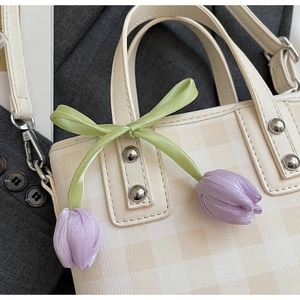 Close-up of beige plaid bucket bag featuring a green ribbon and purple tulip charm detail