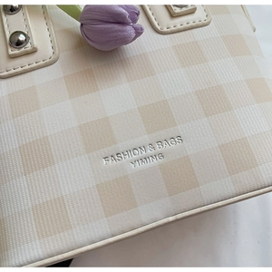 Detail of cream and brown checkerboard bucket bag with silver lettering and metal rivets