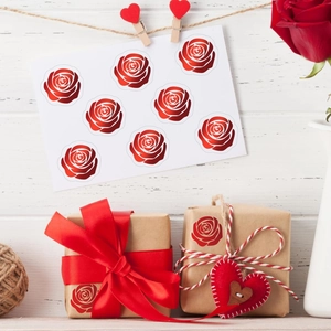 Dettaglio di adesivi rosa rossa usati come sigilli decorativi su scatole regalo in kraft