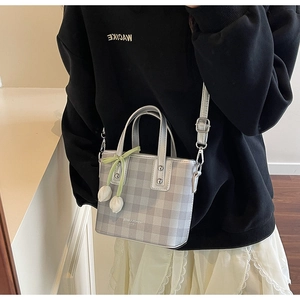 Detail of silver plaid bucket bag featuring a green ribbon bow and floral charms