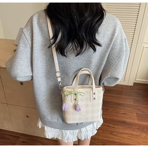 Detail of cream plaid bucket bag featuring purple tulip charm and detachable strap