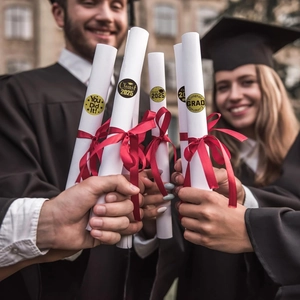 Close-up of Class of 2025 graduation stickers with red ribbons on diploma scrolls