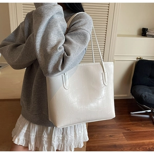 Gros plan d'un sac cabas blanc à motif crocodile porté à l'épaule dans un décor intérieur