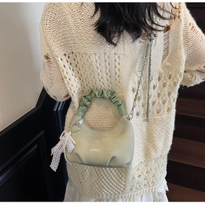 Détail du sac vert clair avec texture tissée, nœud en dentelle et breloque en perle