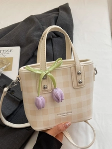 Fashionable beige bucket bag with green ribbon and tulip charm in a handheld view