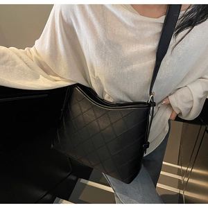 Detail of black rhombus quilted tote bag with wide strap worn by a model in lifestyle setting