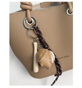 Detail of baseball charm with bat and glove on a beige textured bucket bag
