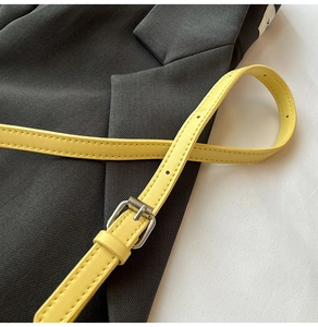 Détail d'une ceinture fine en similicuir jaune vif avec boucle argentée sur un blazer