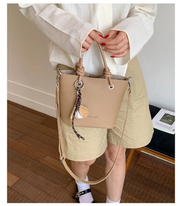 Détail du sac seau marron clair grainé avec charm baseball sur un parquet en bois