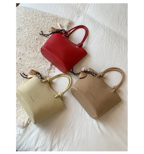Close-up of three elegant bucket bags in red, beige, and brown with lychee grain texture