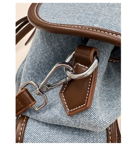 Macro shot of silver metal lobster clasp and brown leather strap on light blue denim bag