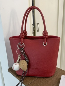 Sac seau rouge en cuir grainé avec porte-clé baseball exposé sur étagère en bois