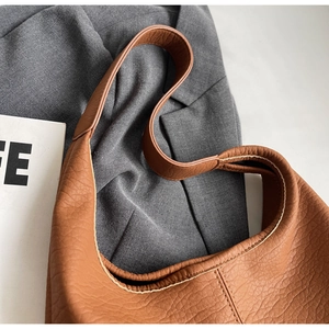 Gros plan sur le sac fourre-tout marron caramel avec texture grainée sur un costume gris
