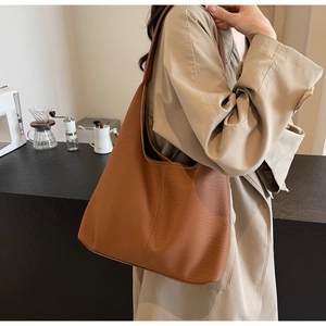 Gros plan du sac hobo en cuir caramel à texture grainée avec un manteau kaki chic