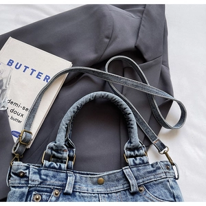 Dettaglio della borsa tote in denim lavato con rivetti vintage su sfondo blazer grigio