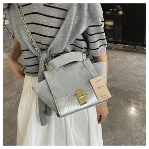 Detail of silver gray matte handbag with embossed crocodile pattern and gold lock buckle